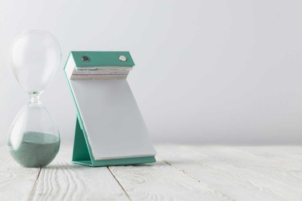 Acercamiento de una libreta de notas parada en una base triangular y un reloj de arena.