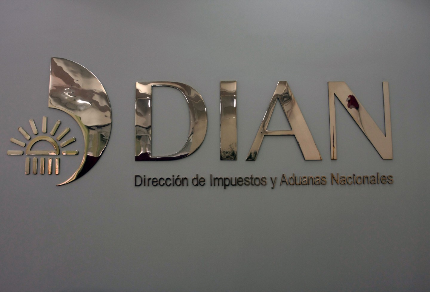 Fotografía del logo de la DIAN en material dorado sobre una pared gris.