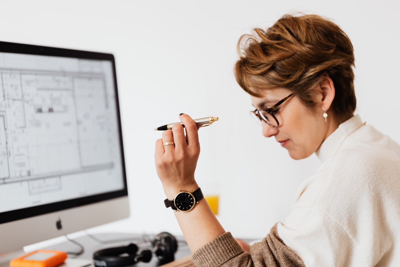 Mujer sentada al frente de un computador, sosteniendo un lapicero y revisando notas.