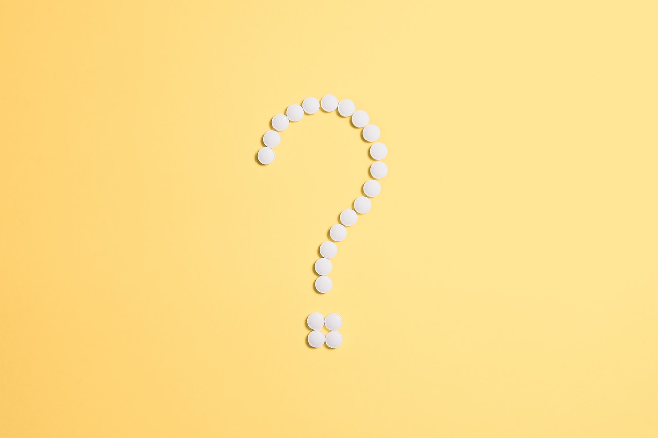 Signo de interrogación formado con píldoras blancas sobre un papel amarillo.