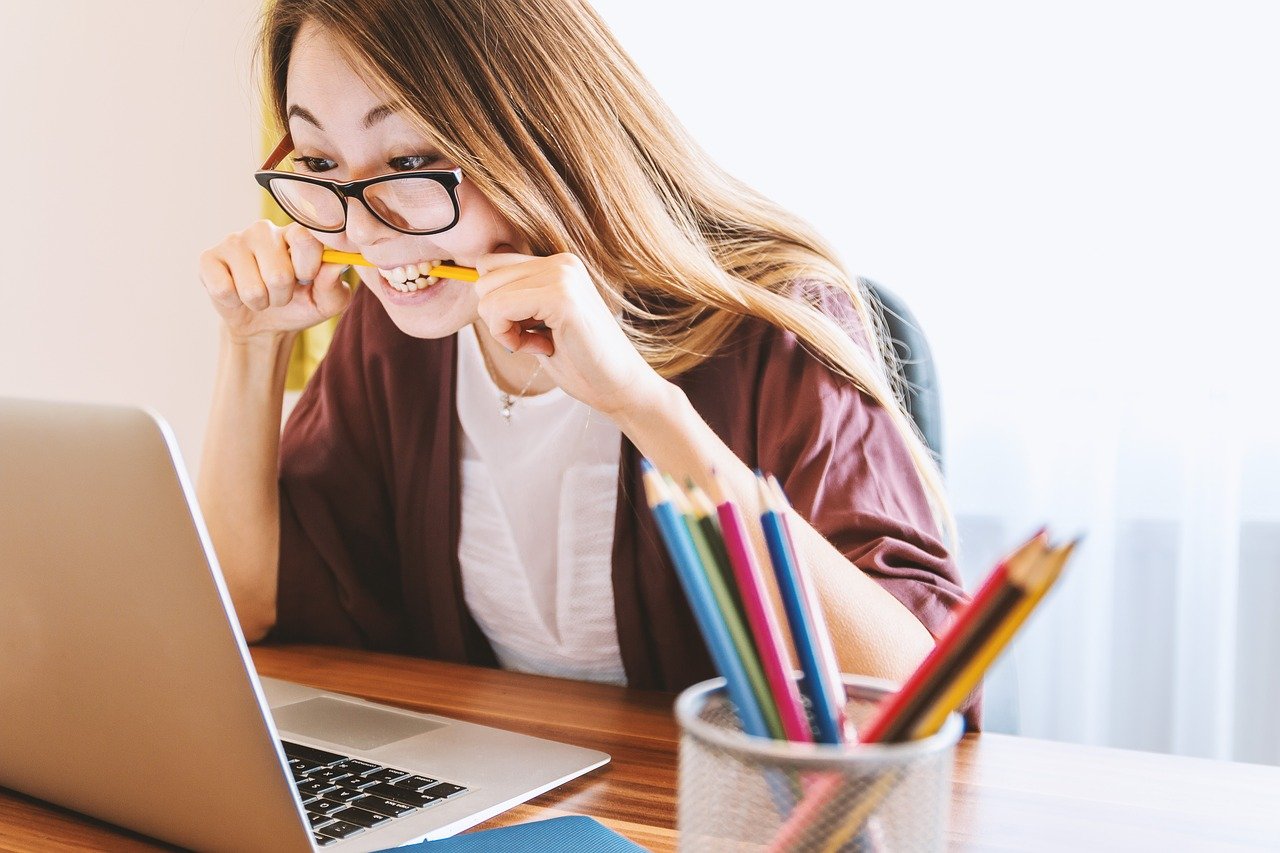Mujer joven sentada al frente de un computador portatil mordiendo un lápiz.
