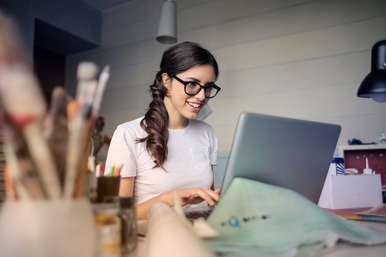 Mujer sentada al frente de un computador escribiendo y sonriendo.