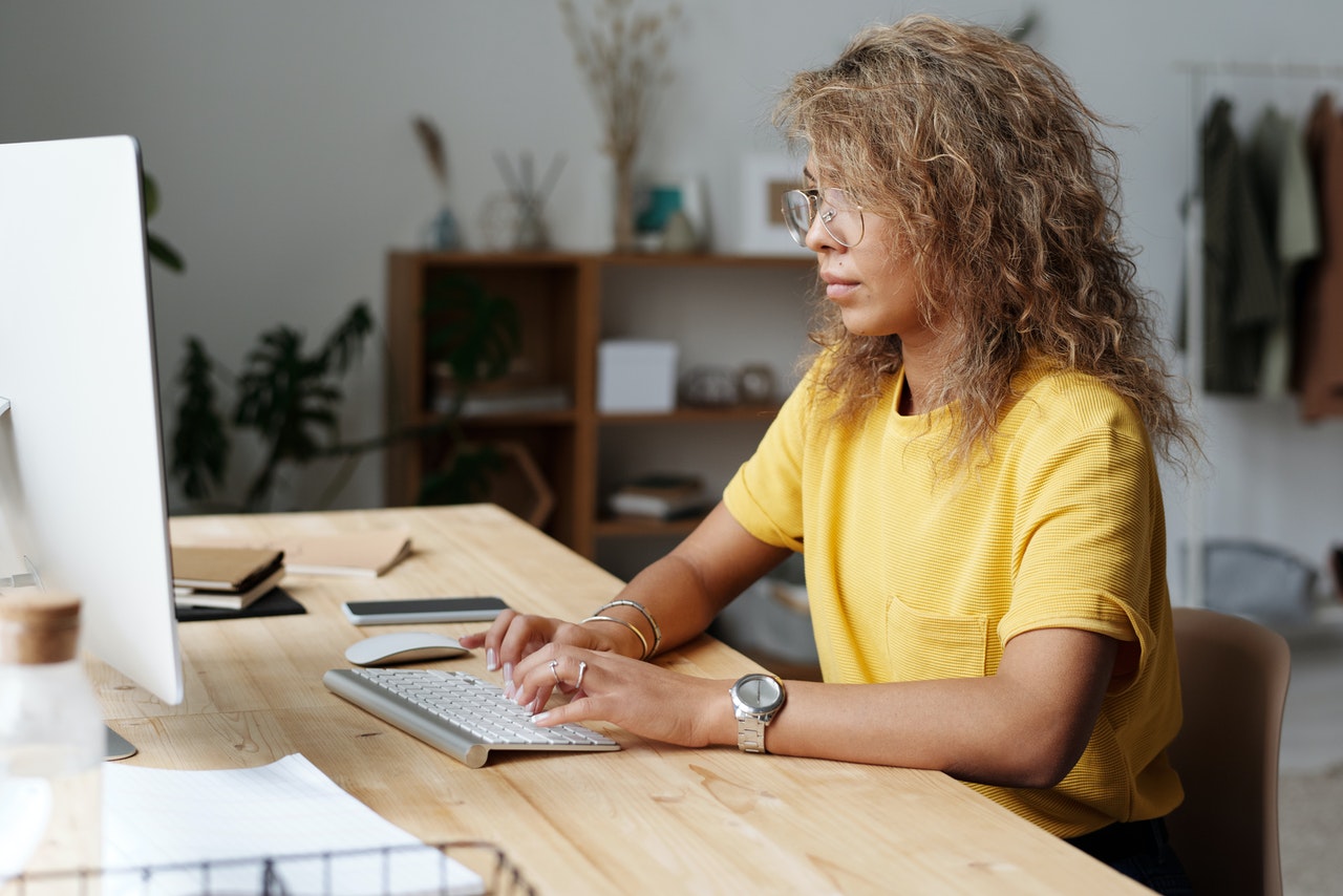 Mujer sentada al frente de un computador escribiendo con el teclado.